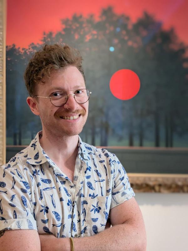 Man with glasses and mustache standing in front of a vivid painting